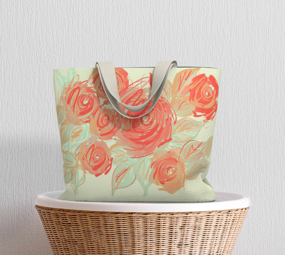 Xyla Sovereign tote bag sitting on wicker table, displaying painterly coral roses with mint and clay accents