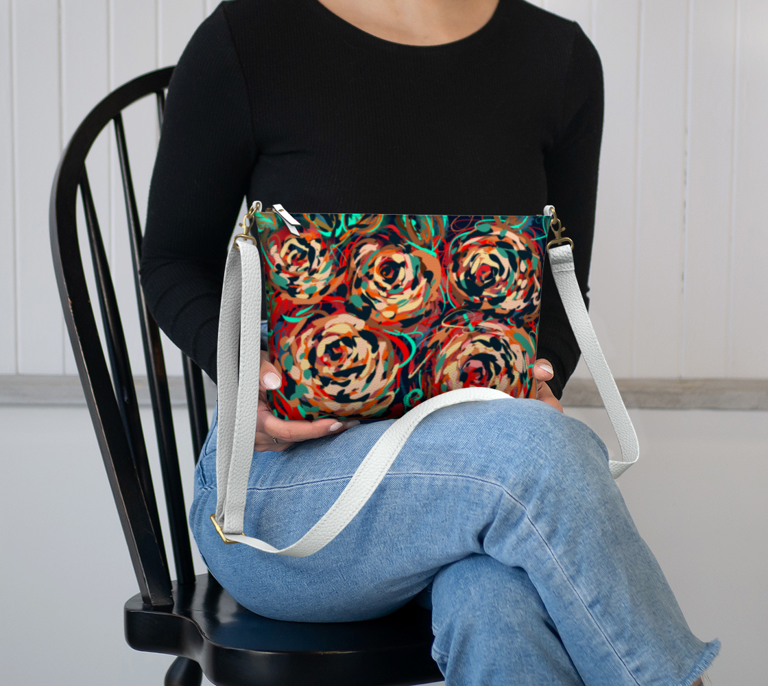 Blythe Collection Vegan Leather Crossbody Purse in Floral Abstract Design sitting in the lap, displaying bold hand-painted roses in red, teal, and earthy tones.